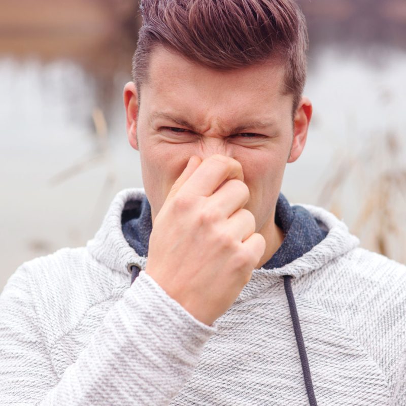Man in hoodie holding nose in front of pond